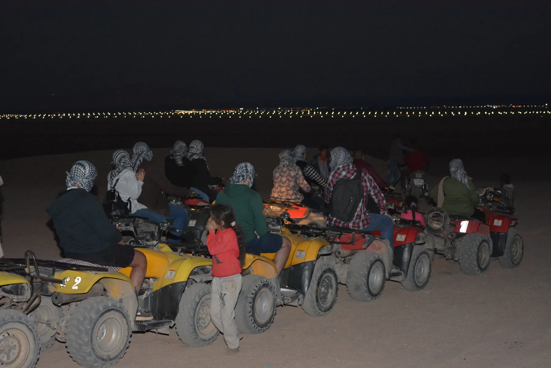 Riders in headscarves lined up on quad bikes at dusk on a desert safari in Egypt.