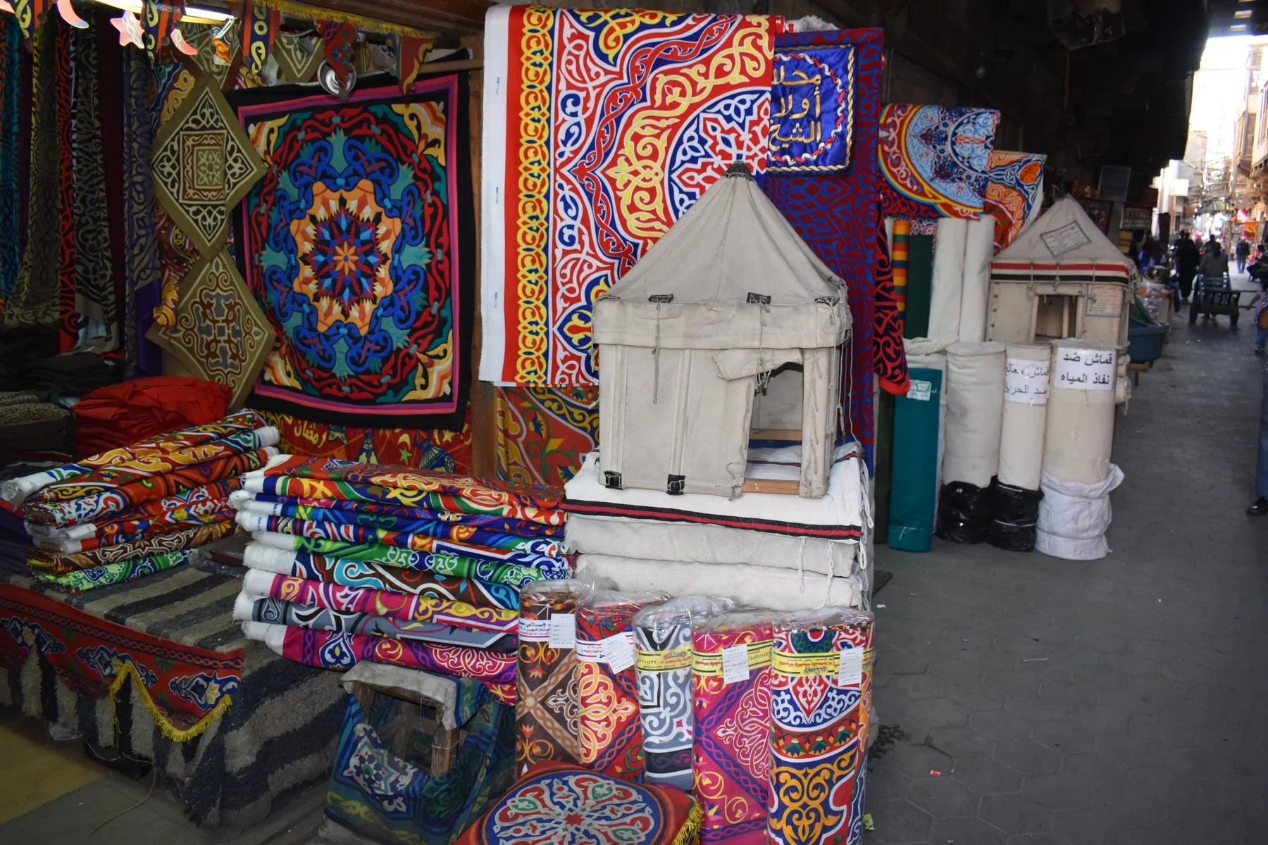 Colourful textile panels, folded cloth and rolls displayed at a shop beside the passage in Elkhiyamia Street.