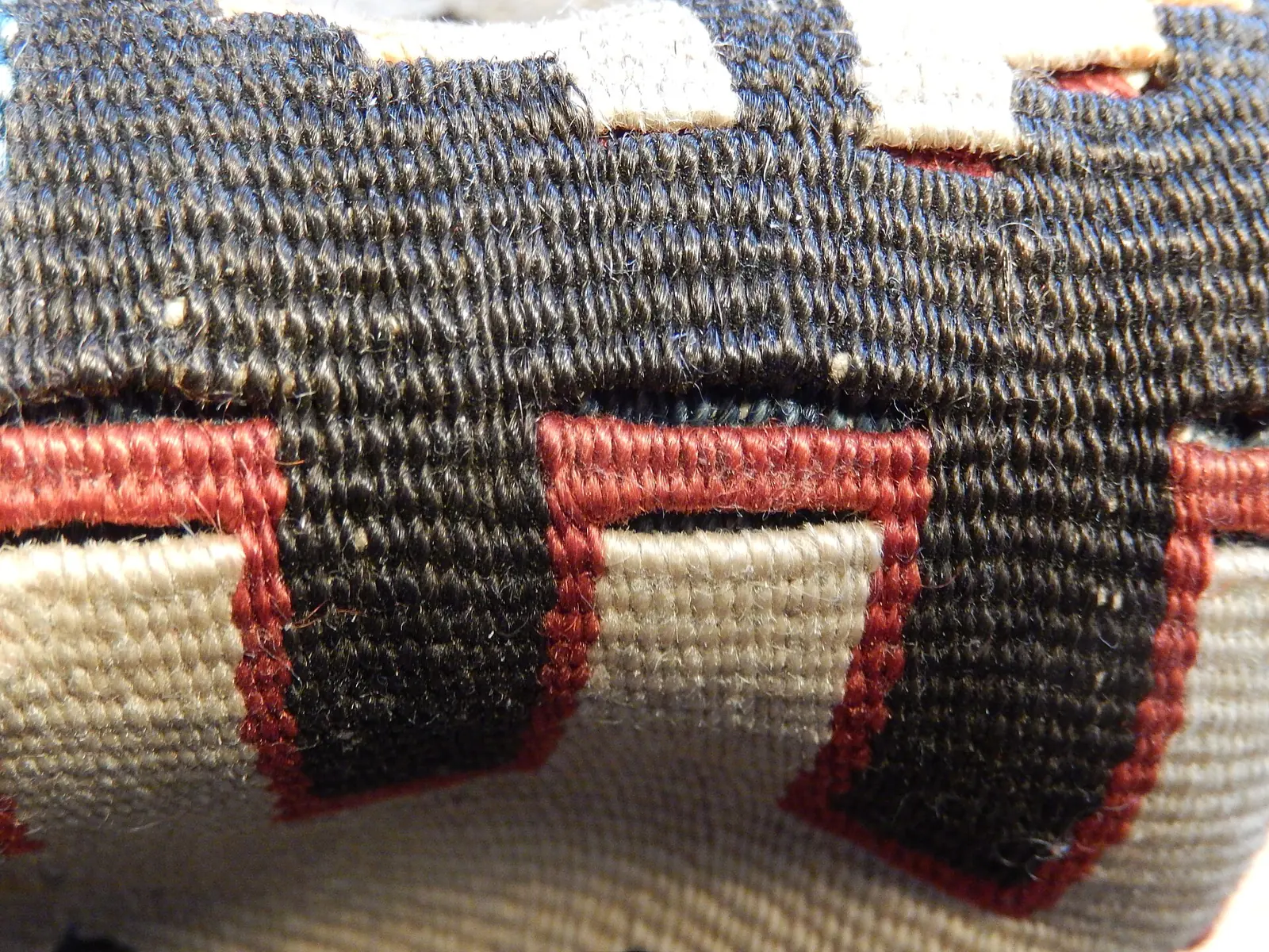 Close view of a folded flat-woven rug: blocks of red, white and dark wool meet at vertical slits where one colour ends and the next begins.