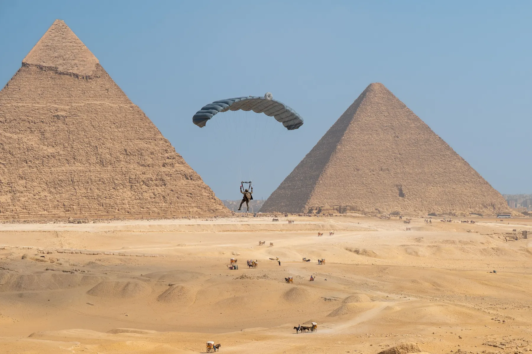 A parachutist under canopy between two of the Giza pyramids during a military freefall display in September 2025.