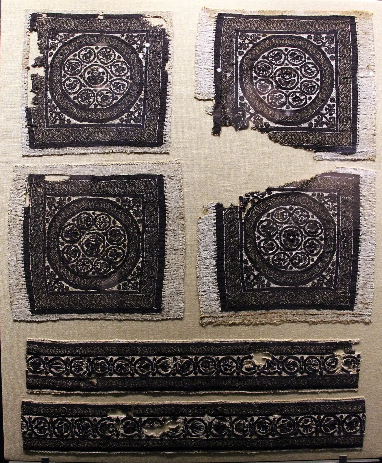 Four tapestry-woven squares, each a roundel of busts and animals in dark purple wool on pale linen, above two narrow woven bands.