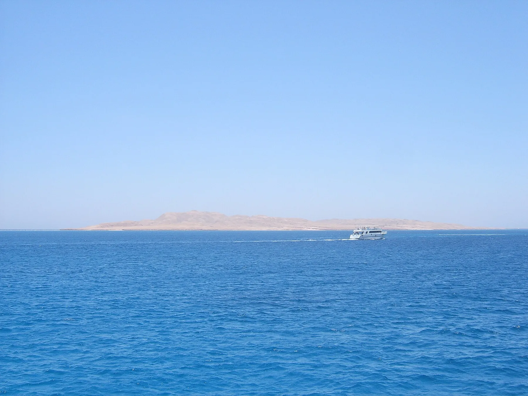 Giftun Island low on the horizon across the blue Red Sea, with a boat passing.