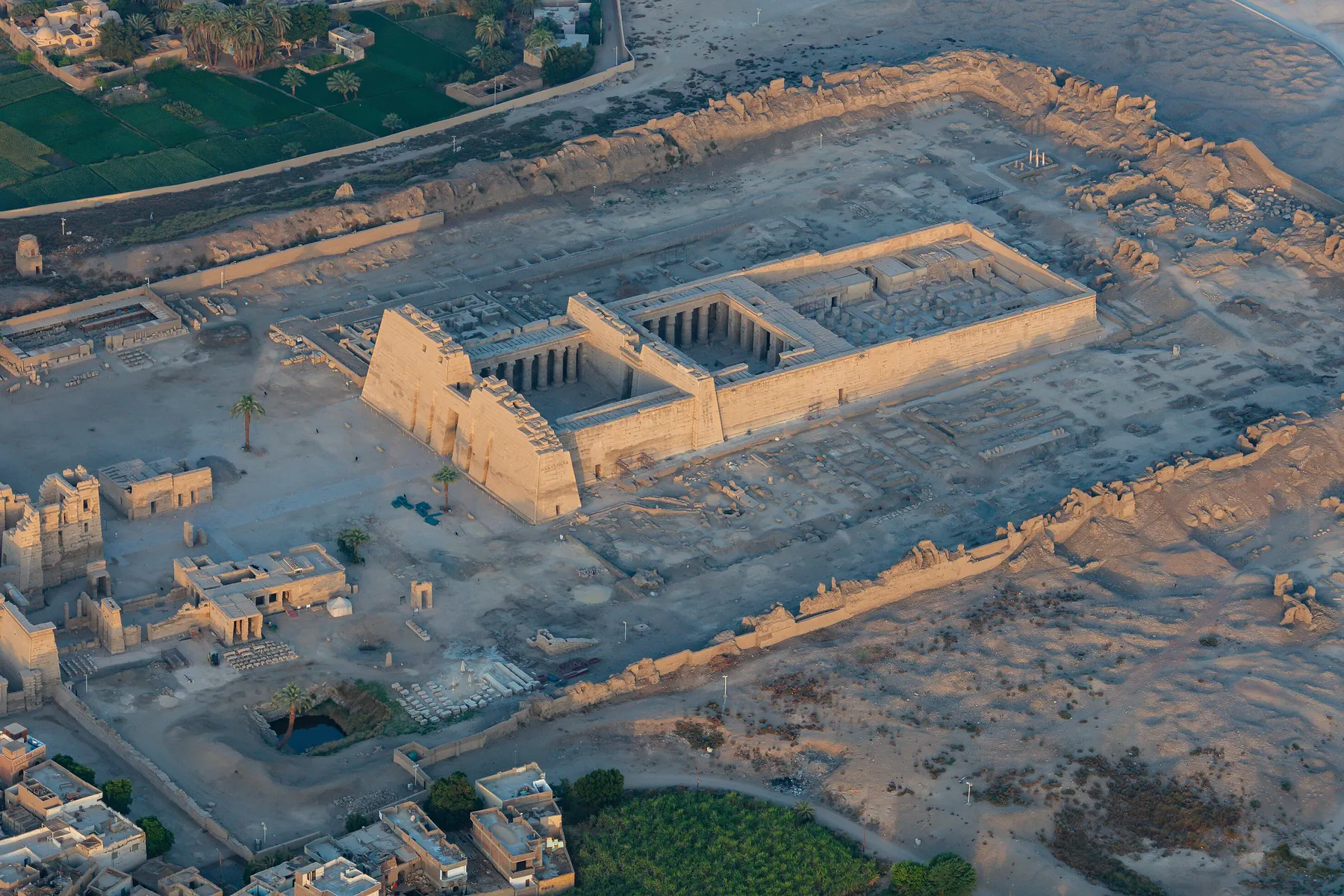 Medinet Habu from the air at sunrise: the pylons and courts of Ramesses III's temple inside the walls of its estate, with the High Gate at the lower left.